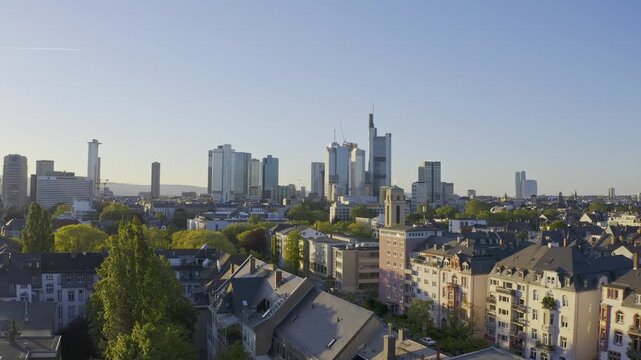Aerial view of the Frankfurt skyline at twilight: Skyscrapers rise above residential areas and parks under a clear sky.