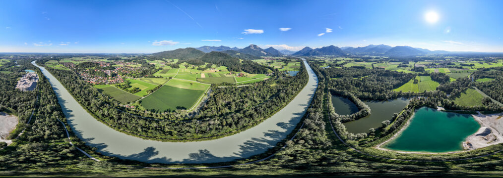 Aerial view of the serene river carves through a landscape of emerald fields and verdant forests under a vast, azure sky, Neubeuern, Bavaria, Germany.