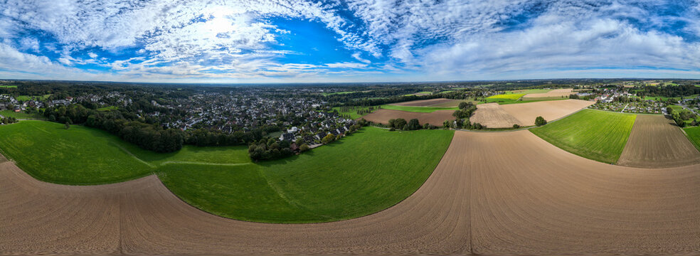 Aerial view of a patchwork of green fields and cultivated land meeting the edge of a town under a sky streaked with clouds, Leichlingen, Germany.