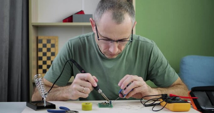 Man repairs circuit board using soldering iron. Focus remains on precision and craftsmanship. Work environment showcases tools like multimeter and wire cutters. Ideal for technology and DIY