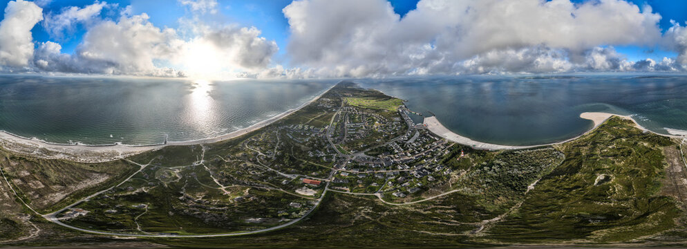 Aerial view of the serene coastline where sandy beaches meet the tranquil sea under a sky brushed with soft clouds, Sylt, Germany.