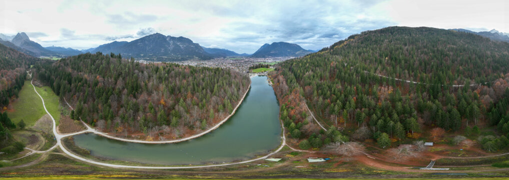 Aerial view of the Rissersee lake nestled between hills with dense forests showing a mix of green and brown hues, Garmisch, Germany.