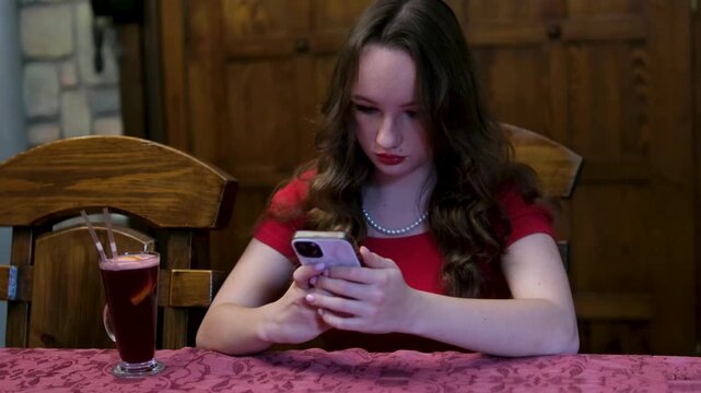 Woman in red dress using smartphone at wooden table dark red room wine drink social media ordering food online