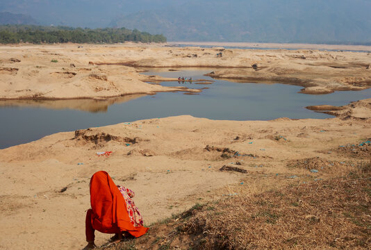 Sunamganj, Bangladesh - 26 January 2019: View of the golden sands of the riverbed contrasting with the clear water, a solitary figure in vibrant orange adding a splash of color.