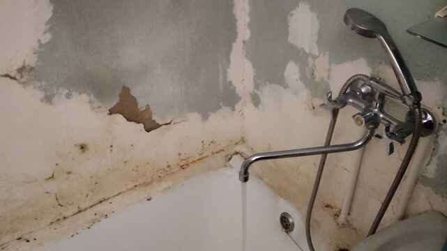 Water flowing from a tap into old, moldy, crumbling, scary bathroom, dirty and shabby