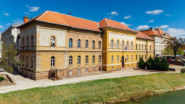 Aerial view of the grand, sunlit facade of a historic building with its orange roof contrasting against the clear blue sky, Zrenjanin, Vojvodina, Serbia.