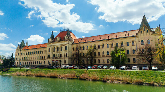 Aerial view of the grand, pale-yellow building with its red-tiled roofs and intricate spires, reflected in the shimmering green waters below, Zrenjanin, Vojvodina, Serbia.