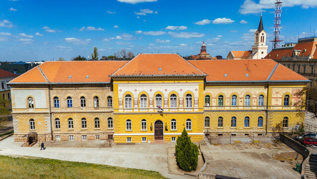 Aerial view of the bright yellow facade of a building, contrasting against the terracotta roof and blue sky, Zrenjanin, Vojvodina, Serbia.