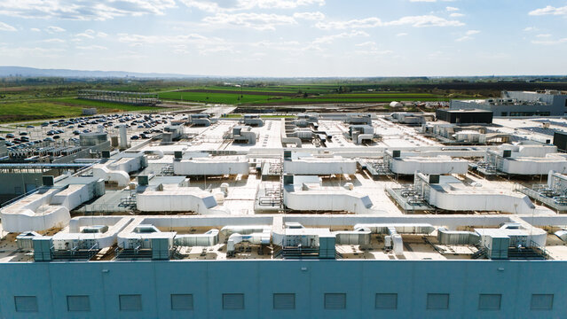 Aerial view of a sprawling industrial complex with a vast rooftop adorned with vents and machinery, contrasting with the distant green fields, Becej, Vojvodina, Serbia.