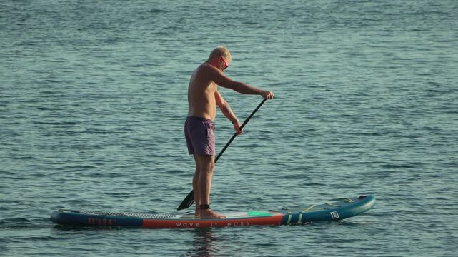 Senior man paddleboarding, calm sea, active lifestyle, summer water sports, healthy leisure activity