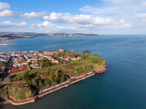 Aerial view of the coastline where the red cliffs meet the turquoise sea, the green vegetation contrasts with the white buildings, Paignton, England, United Kingdom.