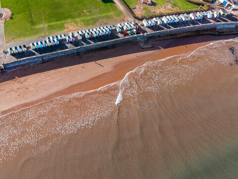Aerial view of the gentle waves caressing the sandy beach beside the colorful beach huts lining the coast, Paignton, England, United Kingdom.