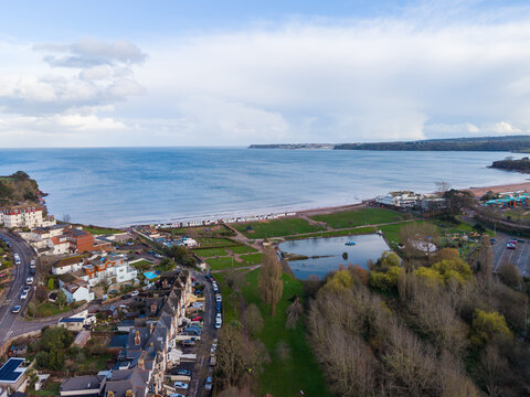 Aerial view of the calm sea meeting the sandy beach, framed by the town's rooftops and lush green spaces, Paignton, England, United Kingdom.