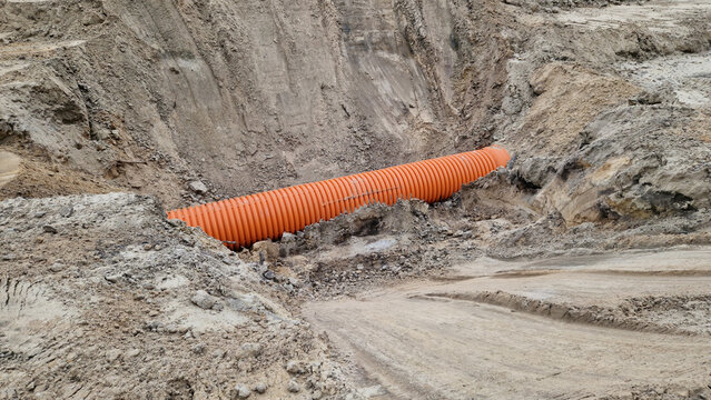 Plastic protective corrugation for cables or drainage laid in sandy soil. The process of underground engineering works. Orange corrugated pipe in a trench at a construction site