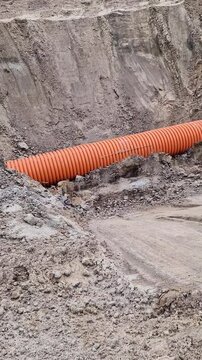 Plastic protective corrugation for cables or drainage laid in sandy soil. The process of underground engineering works. Orange corrugated pipe in a trench at a construction site