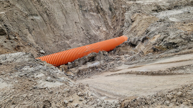 Plastic protective corrugation for cables or drainage laid in sandy soil. The process of underground engineering works. Orange corrugated pipe in a trench at a construction site