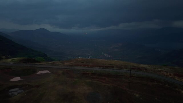 Moving drone shot of dark monsoon clouds over a valley with mountain top in the foreground shot after sunset. Dramatic scene. 4K30fps