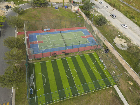 Aerial view of vibrant sports courts, a dynamic mix of basketball and soccer fields, side by side, creating a colorful contrast against the lush greenery, Lekki, Lagos, Nigeria.