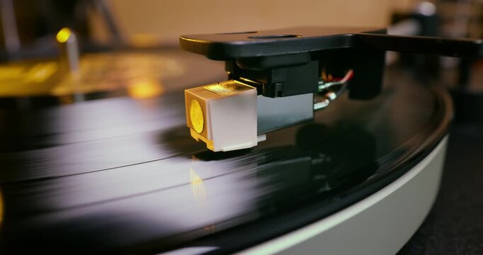 Detailed close-up of a turntable tonearm with white cartridge headshell, positioned over a black vinyl record on the platter, highlighting audio equipment precision.
