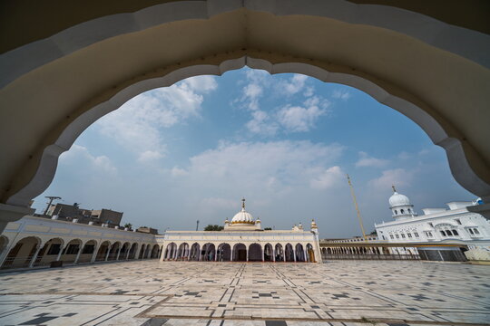 View of white marble gleams under a vast sky, framed by archways, leading to a serene gurdwara complex in Nankana Sahib, Punjab, Pakistan.