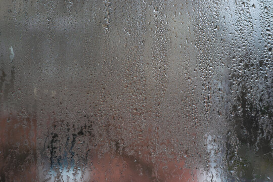 Wet glass covered by moisture and flowing water streaks. glass turning urban view into abstract backdrop. Wet window surface with drop pattern, rainy weather concept, soft blur, closeup texture,
