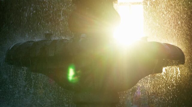 Dramatic close-up of fountain spraying water droplets backlit by bright golden sunlight creating beautiful lens flare effects. Silhouette of ornate fountain structure with mist and sparkling water.