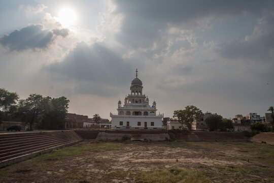 View of the Gurdwara bathed in ethereal sunlight filtering through dramatic clouds, a serene tableau of faith and history, Nankana Sahib, Punjab, Pakistan.