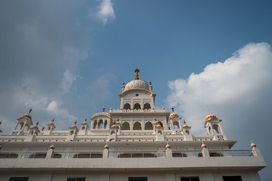 View of a gleaming white building with ornate domes reaching towards the partly cloudy sky, standing as a testament to cultural heritage, Nankana Sahib, Punjab, Pakistan.