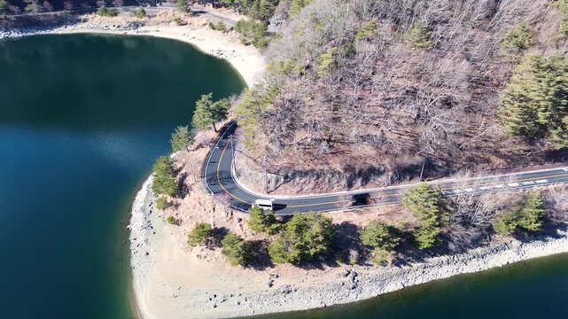 Drone aerial landscape of two van vehicles driving along a scenic highway road around a corner bend surrounded by forest woodland trees near Lake Saiko Mount Fuji Yamanashi Japan Asia transport travel
