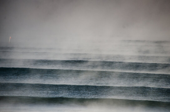 View of the dark and moody ocean, with mist rising off the cold water in horizontal bands of textured blues and greys, , Hossegor, France.