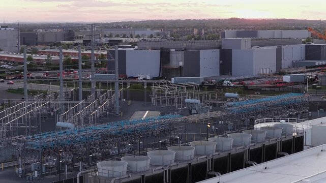 Descending aerial drone shot of large data center campus in Ashburn, Virginia at sunset, featuring cooling infrastructure, power systems and surrounding roads in major USA cloud computing hub. 
