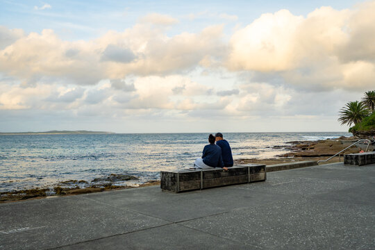 Couple sitting on the waterfront promenade overlooking the ocean at Cronulla, Sydney, Australia