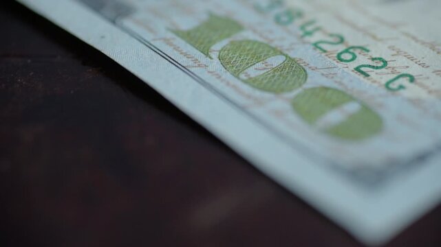 Closeup corner of hundred dollar bill, macro texture of green security ink and serial numbers, paper fibers visible, still arrangement on dark surface, quiet savings mood, high