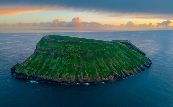 Aerial view of Ilheus das Cabras islet, a verdant jewel amidst the deep blue embrace of the Atlantic, under the pastel hues of dawn, Terceira, Azores, Portugal.