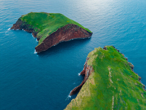 Aerial view of the striking contrast of green vegetation and red volcanic rock on the Ilheus das Cabras islands against the deep blue sea, Ilheus das Cabras, Terceira, Azores, Portugal.