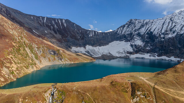 Aerial view of the serene lake mirroring the sky, cradled by rugged, snow-dusted mountains, a symphony of blues, browns, and whites, Neelum Valley, Azad Kashmir, Pakistan.