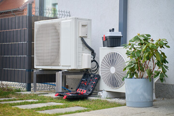 Outdoor heat pump units beside house with open toolbox and tools on ground. Concept of HVAC maintenance, residential climate control, repair and energy efficiency © Lazy_Bear