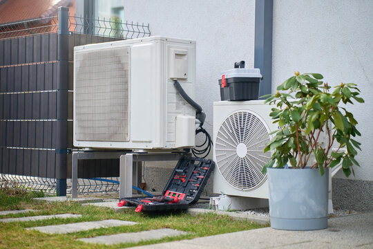 Outdoor heat pump units beside house with open toolbox and tools on ground. Concept of HVAC maintenance, residential climate control, repair and energy efficiency