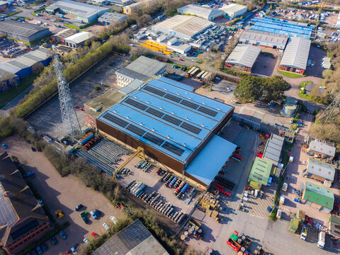 Aerial view of industrial buildings with solar panels glinting under the sun, surrounded by lush trees, Exeter, England, United Kingdom.