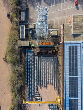 Aerial view of neatly stacked metal bars casting long shadows beside a towering antenna and industrial buildings, Exeter, England, United Kingdom.
