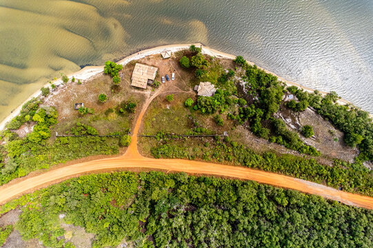 Aerial view of the red earth road splitting through the lush green forest leading to the beachside huts, Monrovia, Liberia.