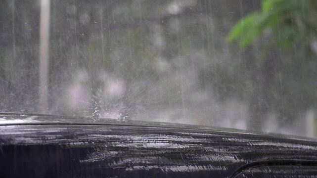 Rain falls on a wet car roof with droplets splashing in a natural outdoor scene