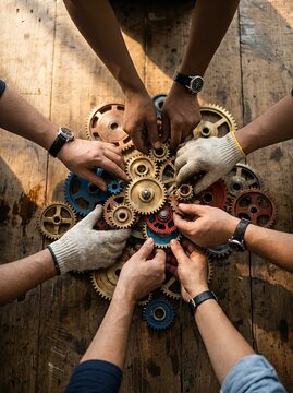 Multiple hands collaborate to fit various colored gears on a wooden surface, symbolizing teamwork and unity.