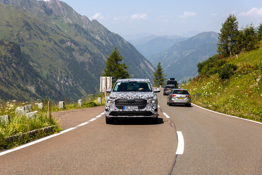 High Alpine Road, Austria - July 31, 2024. Camouflaged Audi prototype drive along alpine road green mountains deep valley clear sky. Scenic european landscape traffic mountain pass automotive testing