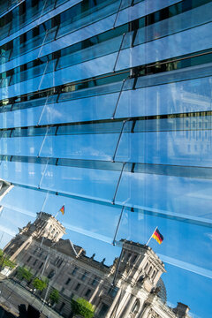 Modern glass reflection frames Berlin Reichstag with flag showing urban landmark architecture in Germany with bold geometric pattern in daylight