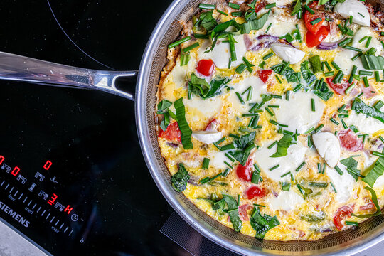 Cooking an italian frittata with mozarella, asparagus, eggs, onions, tomatoes and fresh herbs in spring time at home in the kitchen