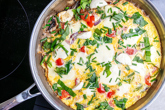 Cooking an italian frittata with mozarella, asparagus, eggs, onions, tomatoes and fresh herbs in spring time at home in the kitchen