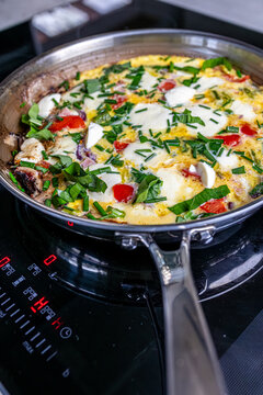 Cooking an italian frittata with mozarella, asparagus, eggs, onions, tomatoes and fresh herbs in spring time at home in the kitchen
