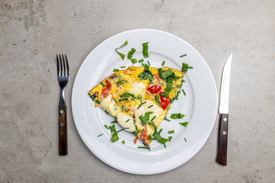 Cooking an italian frittata with mozarella, asparagus, eggs, onions, tomatoes and fresh herbs in spring time at home in the kitchen