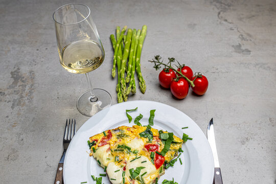 Cooking an italian frittata with mozarella, asparagus, eggs, onions, tomatoes and fresh herbs in spring time at home in the kitchen